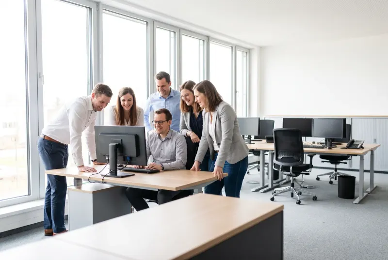 Sechs Verkäufer drängen sich um den einen Schreibtisch mit Zugang, während ihre eigenen Plätze dahinter leer stehen