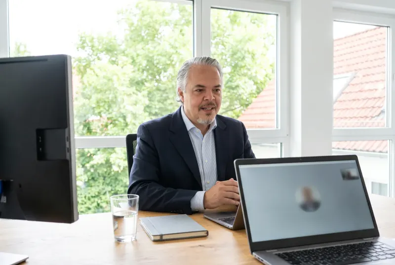 Alvaro Moreno sitzt am Schreibtisch im hellen Büro und spricht ruhig in eine Videokonferenz