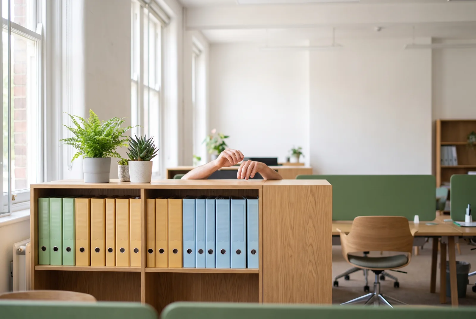 Helles Büro am Mittag, Hände greifen nach einem von mehreren beschrifteten Ordnern in einem offenen Regal